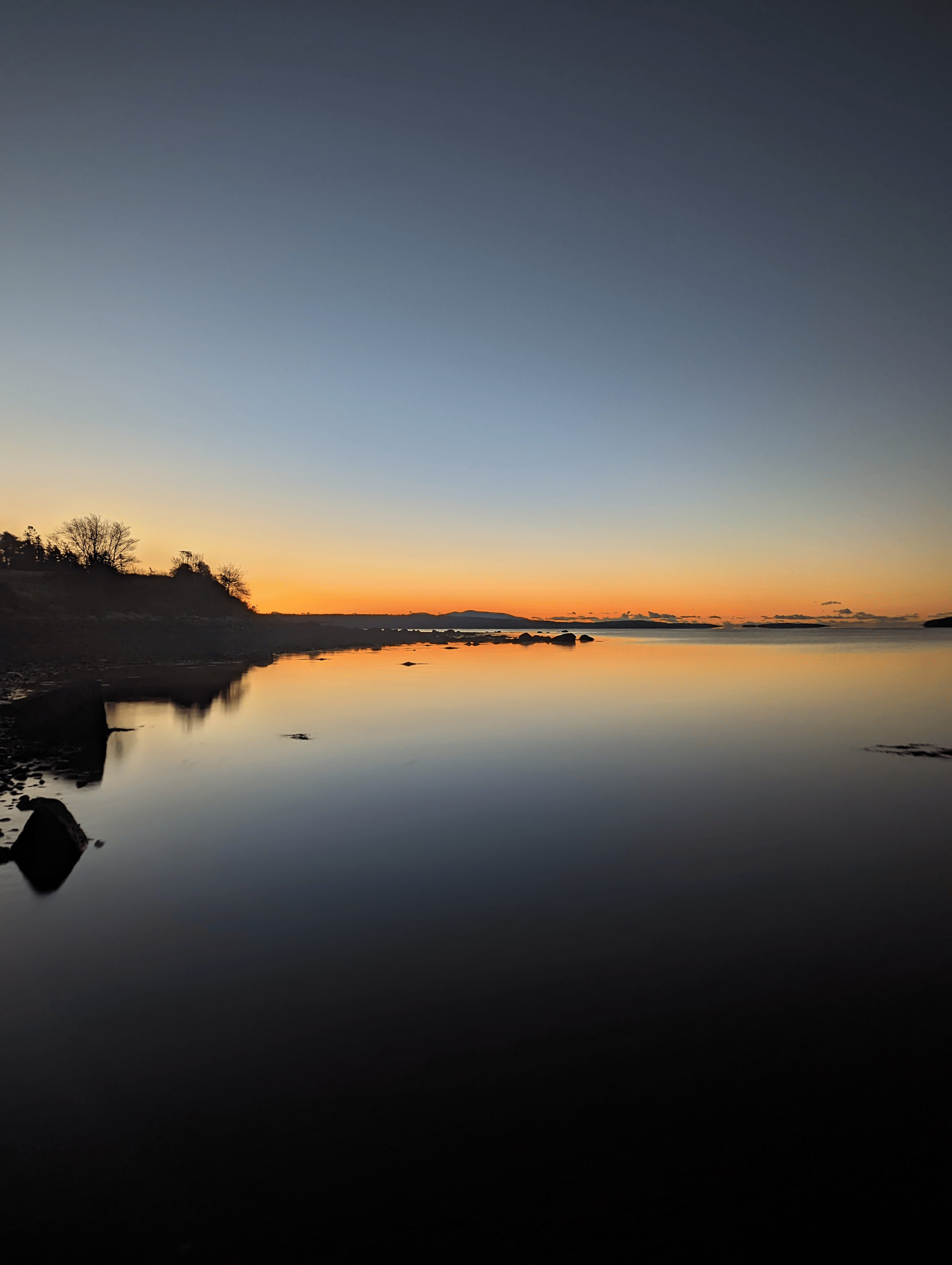 Sunset over still water on the Downeast Maine coast, amber light fading to deep blue with granite silhouettes at the shoreline